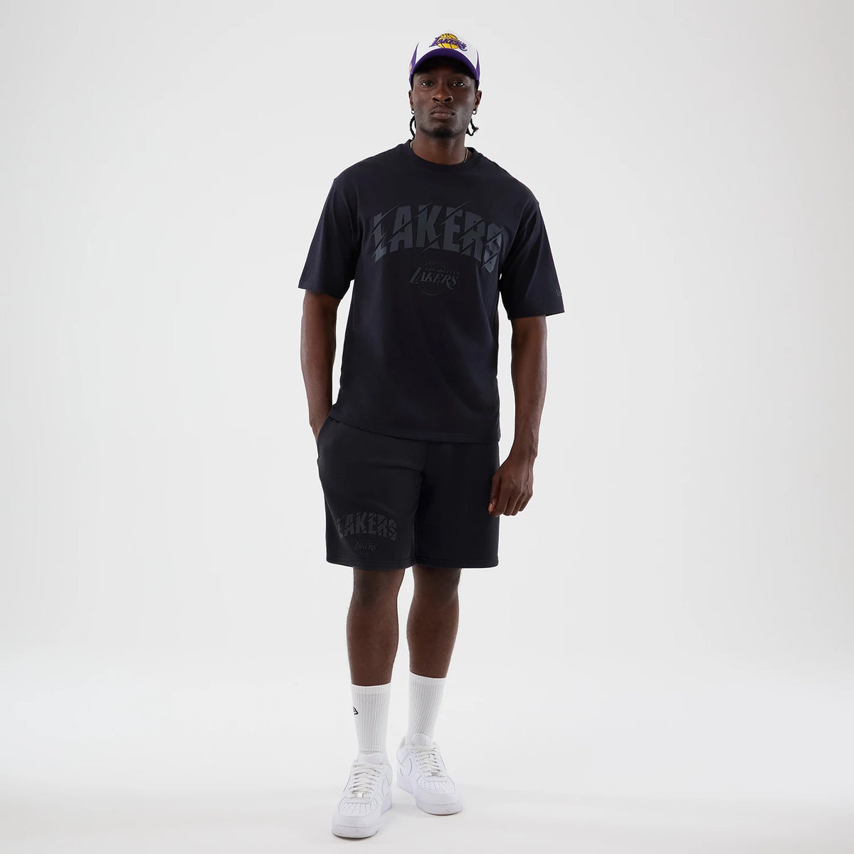 New Era LA Lakers NBA Core Plus Navy Oversized T-Shirt, front view on-model featuring Lakers lettering across the chest, paired with matching shorts showcasing a similar design, and styled with a cap and white trainers.