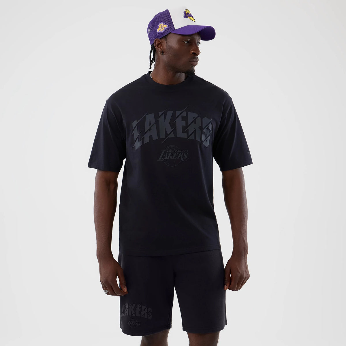 New Era LA Lakers NBA Core Plus Navy Oversized T-Shirt, front view on a model styled with shorts, showing a large Lakers print across the chest and the official team logo beneath, along with dropped shoulder seams for a relaxed fit.