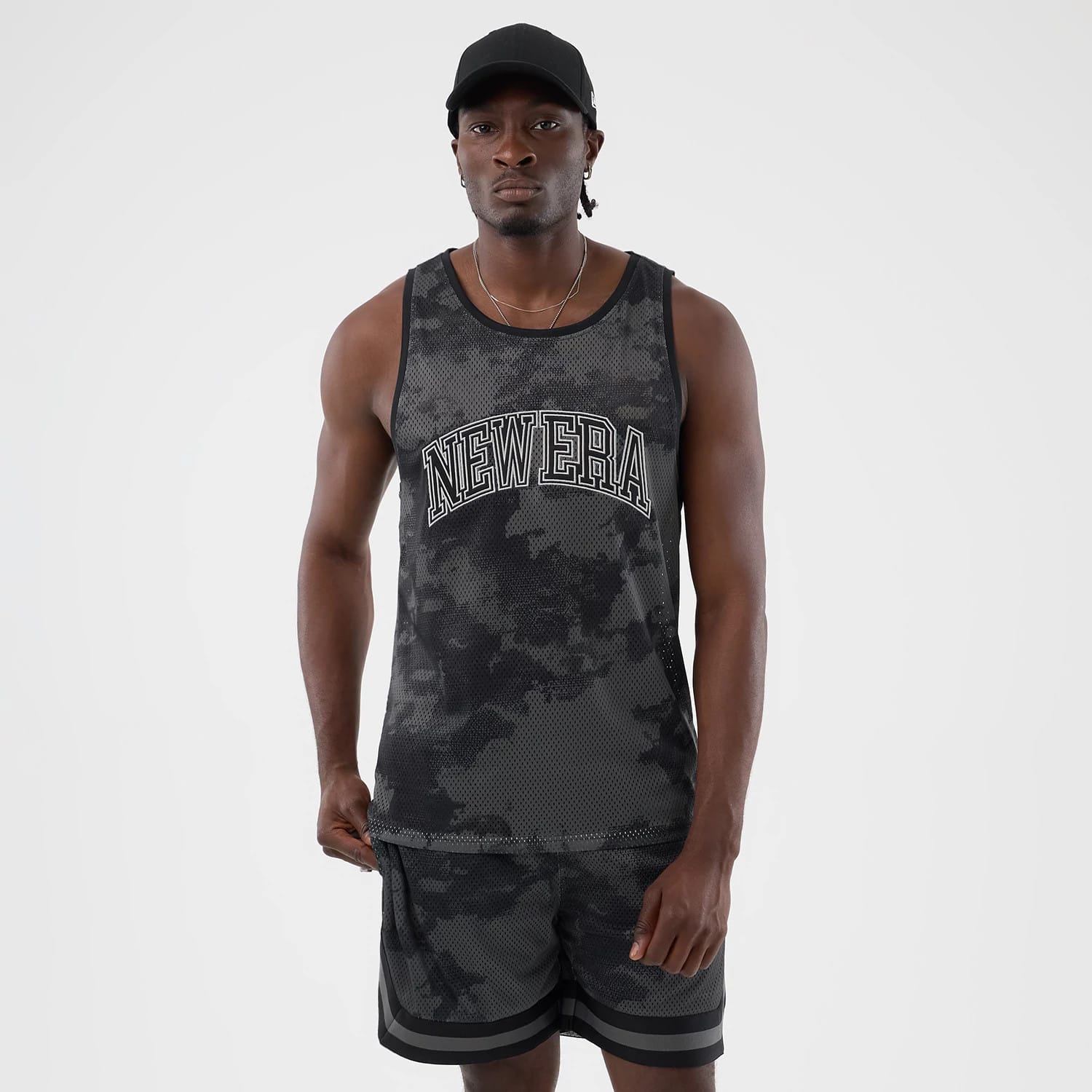 The model is wearing this New Era All Over Print Mesh Tank Top in black camo. 1