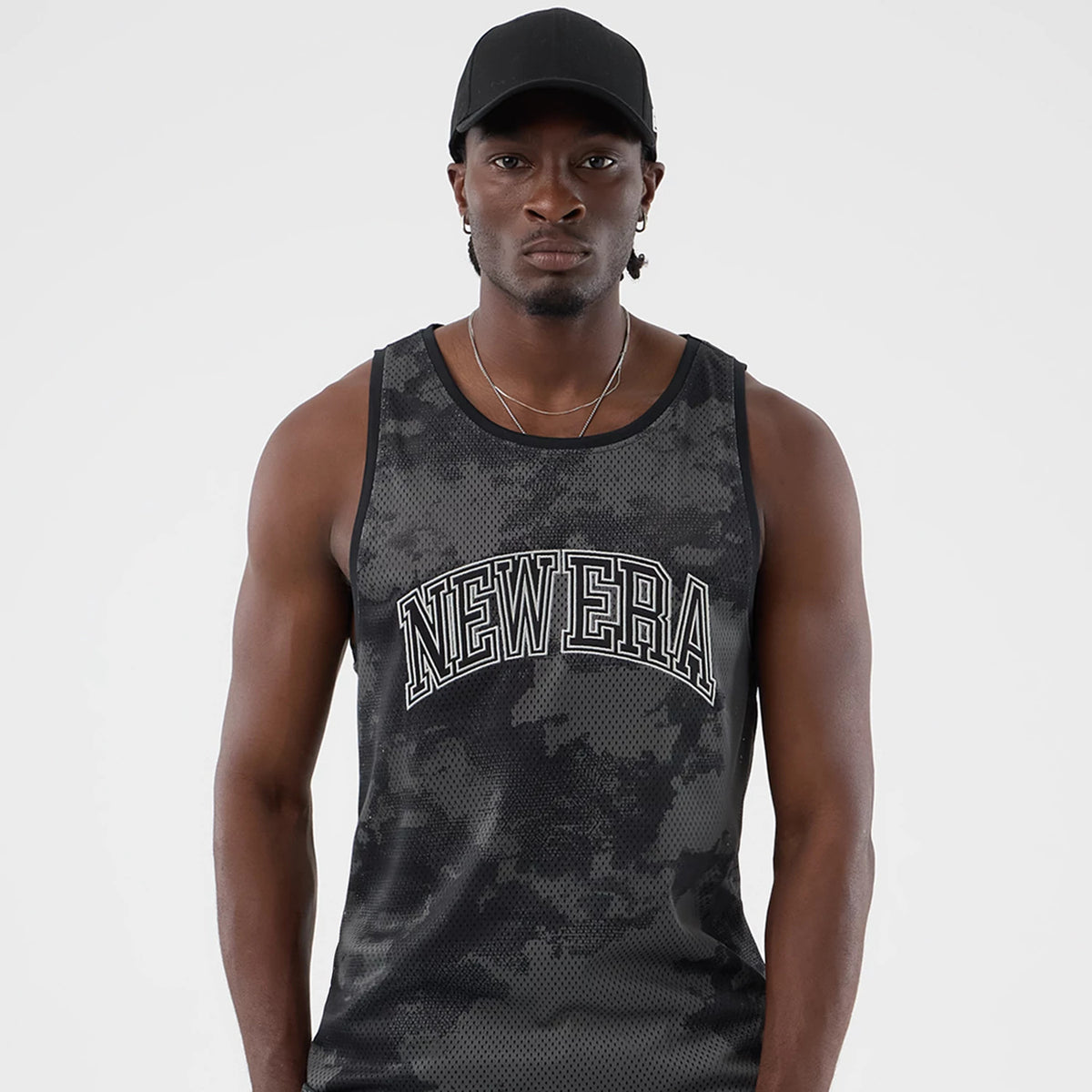New Era All Over Print Black Camo Mesh Tank Top, front view on a model wearing a black cap, showing white NEW ERA lettering across the chest on a black and grey camo pattern, with a sleeveless design.