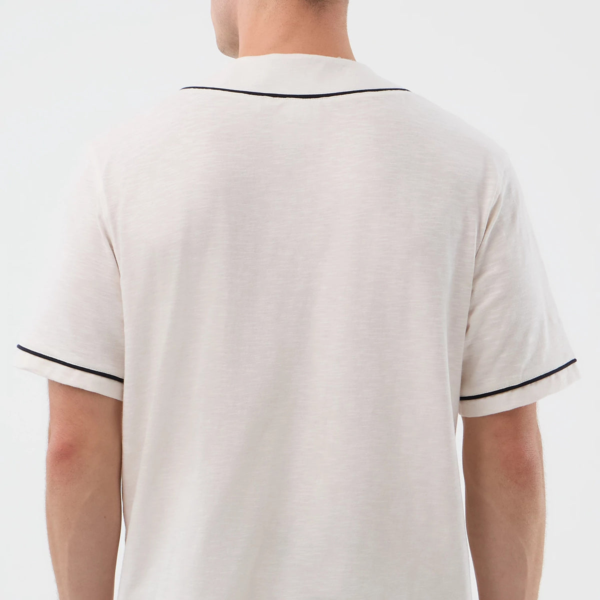 New Era Slub Open White Baseball Jersey, back view on a model showcasing the soft textured slub fabric with contrasting black piping along the collar and sleeve edges, providing a classic and look to the plain white design.