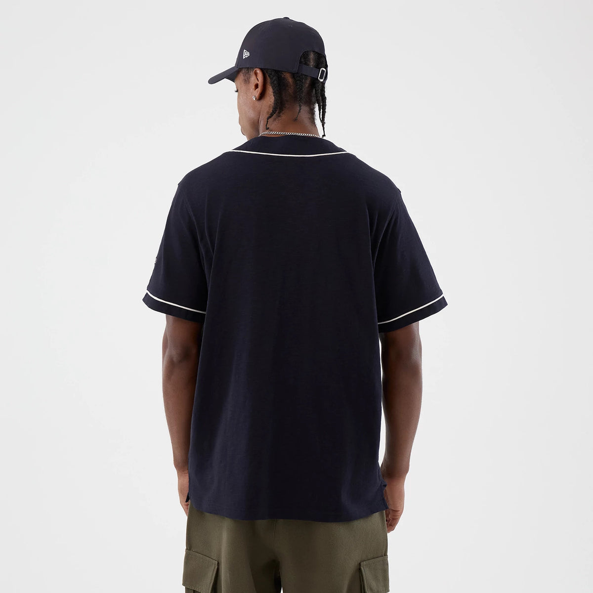 New Era Slub Navy Baseball Jersey, back view on a model with a matching navy cap, featuring white piping along the collar and sleeve edges, creating a classic baseball aesthetic with its soft fabric and relaxed fit.