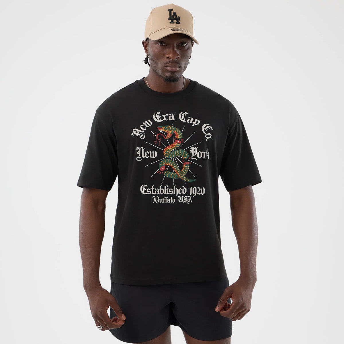 New Era Serpent Graphic Black Oversized T-Shirt, front view on-model showcasing a graphic with a coiled serpent and vintage-style text reading New Era Cap Co New York Established 1920 Buffalo USA centred on the chest.