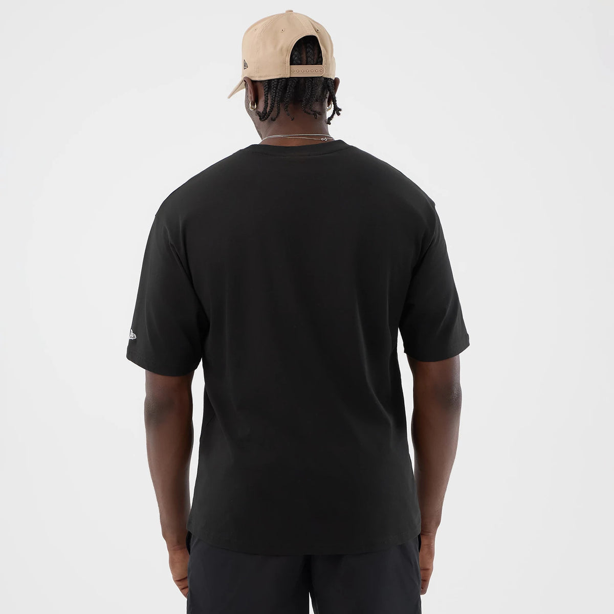 New Era Serpent Graphic Black Oversized T-Shirt, back view on a model showing the plain back with a slightly curved hem, the right sleeve with an embroidered New Era logo, and a neutral cap worn backwards adding to the casual look.