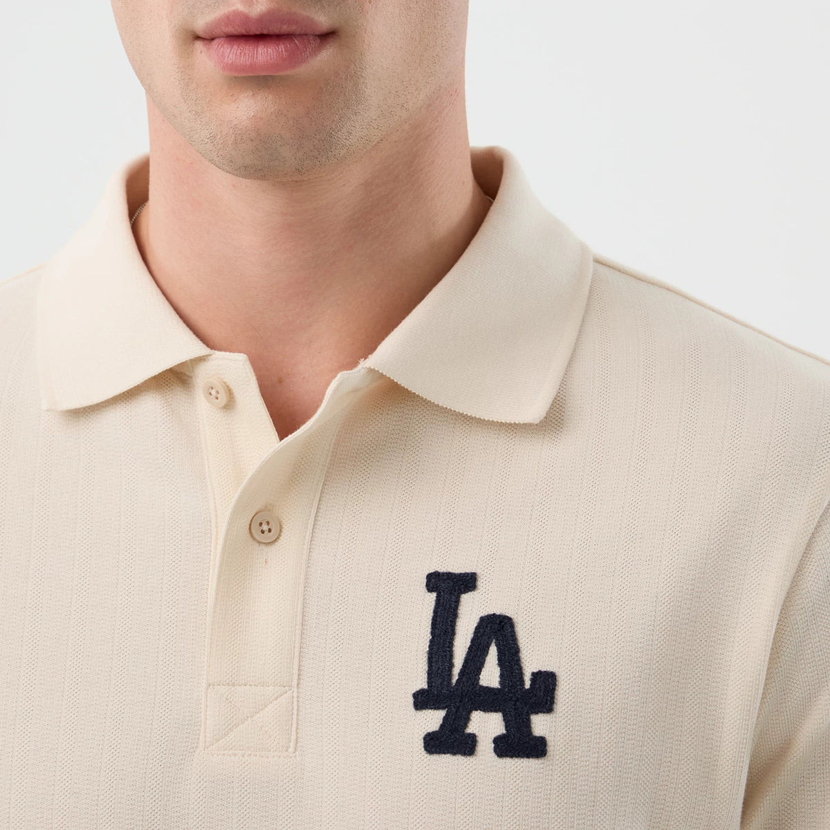New Era LA Dodgers MLB Rib Open White Polo T-Shirt, front view on-model featuring a ribbed texture with a classic collar, two-button placket, and a navy blue embroidered LA logo prominently displayed on the left chest.