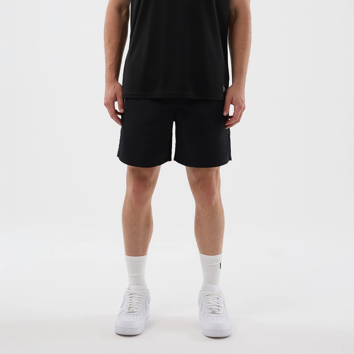 New Era New York Yankees MLB Core Plus Black Shorts, front view on a model styled with a plain black top and white trainers, showing the simple black design with a embroidered New Era logo near the hem on one leg.