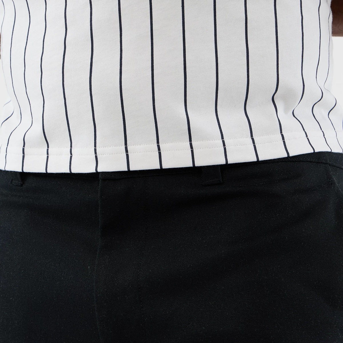 New Era Black Cargo Shorts, front view on a model, displaying the black fabric with belt loops at the waistband and tailoring, styled with a white shirt featuring slim black vertical pinstripes.
