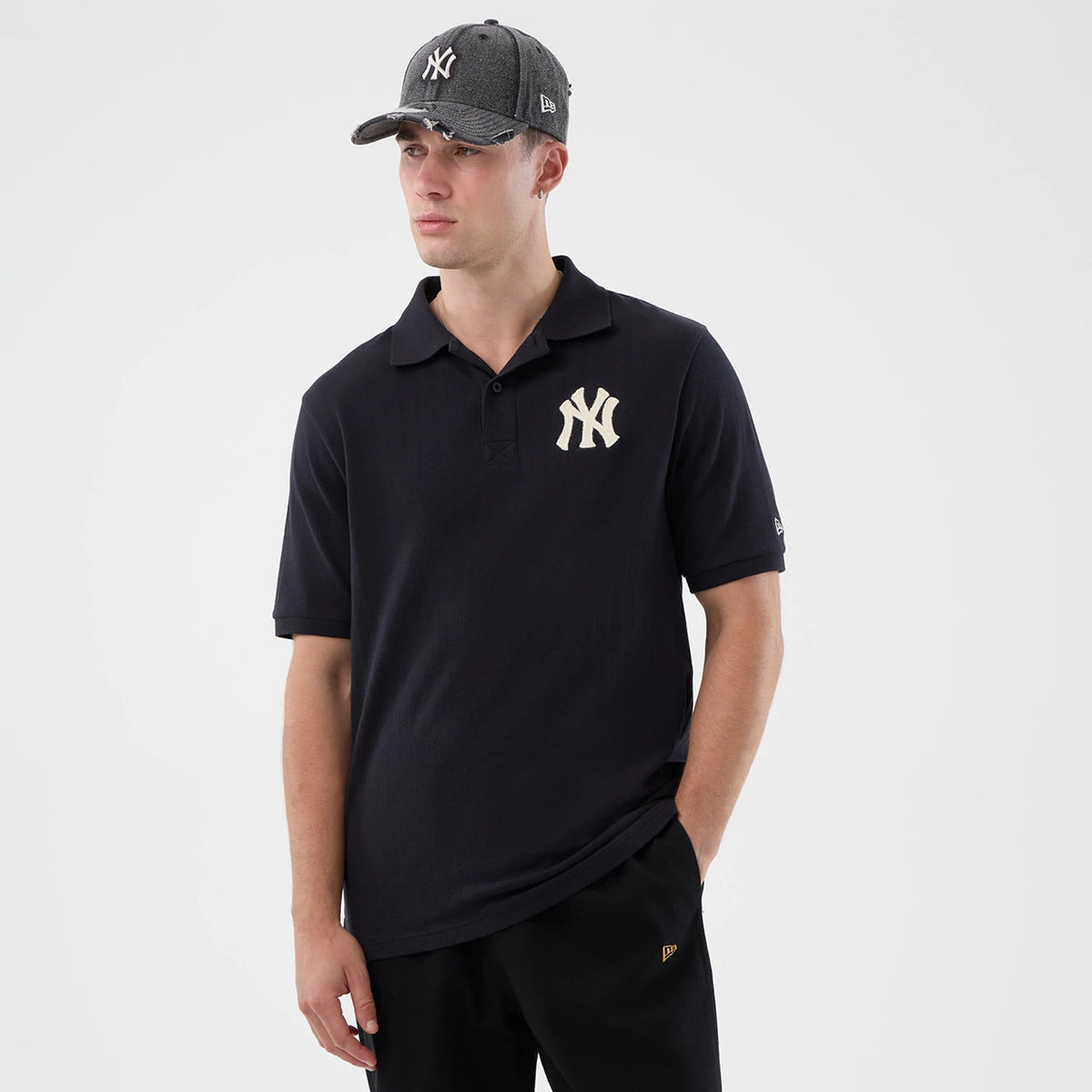 New Era New York Yankees MLB Rib Navy Polo T-Shirt, front view on-model showing a classic polo design with a large, cream embroidered Yankees logo on the left chest, complemented by a matching cap and branding on the left sleeve.