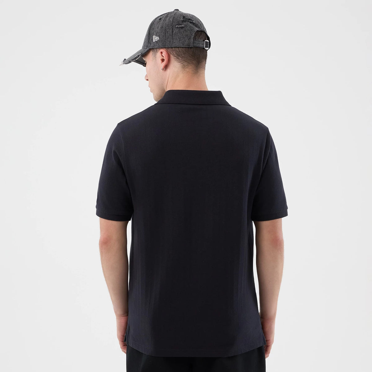 New Era New York Yankees MLB Rib Navy Polo T-Shirt, back view on a model showing the plain navy back with a classic polo collar, short sleeves, and a relaxed fit, complemented by a grey cap with an embroidered New Era logo on the side.