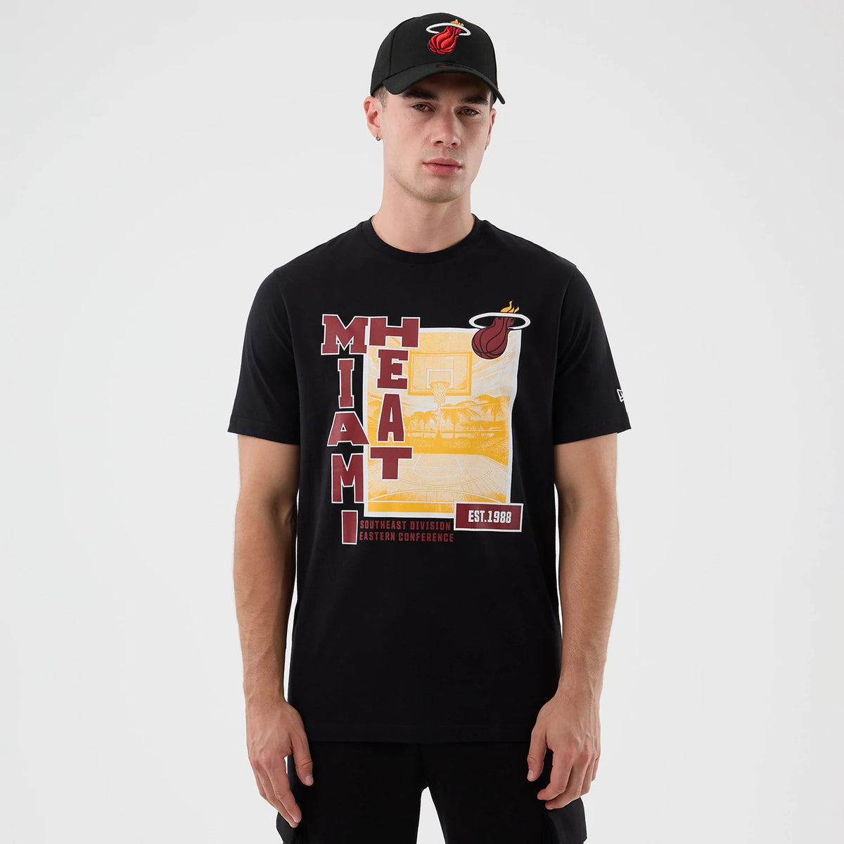 New Era Miami Heat NBA Graphic Black T-Shirt, front view on-model showcasing a graphic with Miami Heat lettering in red and yellow, a basketball court illustration, the Heat logo above, and a small New Era logo embroidered on the left sleeve.