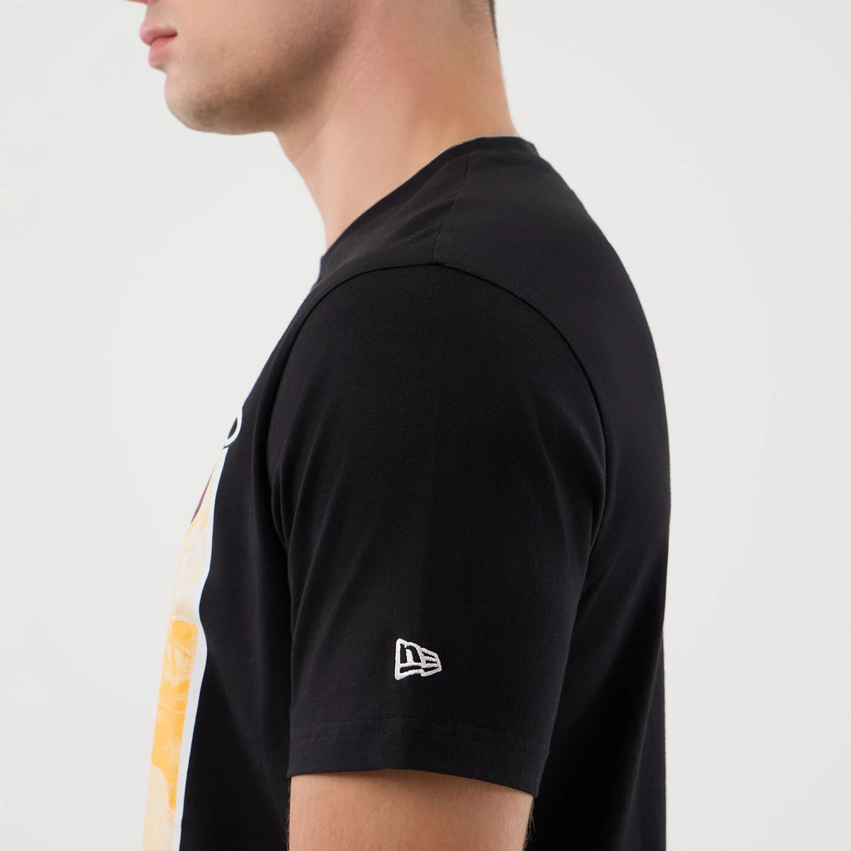 New Era Miami Heat NBA Graphic Black T-Shirt, side view on a model showing the sleeve with an embroidered white New Era logo close to the hem, and part of the colourful front graphic around the side.