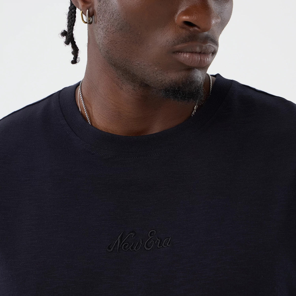 New Era Slub Navy Oversized T-Shirt, front view on a model showing a textured navy t-shirt with an embroidered New Era logo centred on the chest below the round collar, paired with a simple chain necklace.