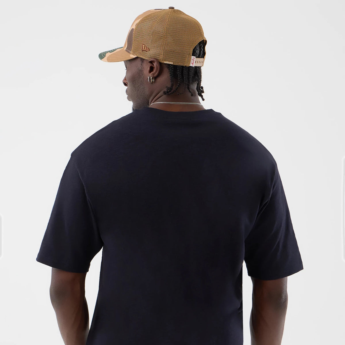 New Era Slub Navy Oversized T-Shirt, back view on a model wearing a tan mesh cap, showing the plain navy back of the oversized fit, with short sleeves and a seam along the shoulders for classic casual styling.
