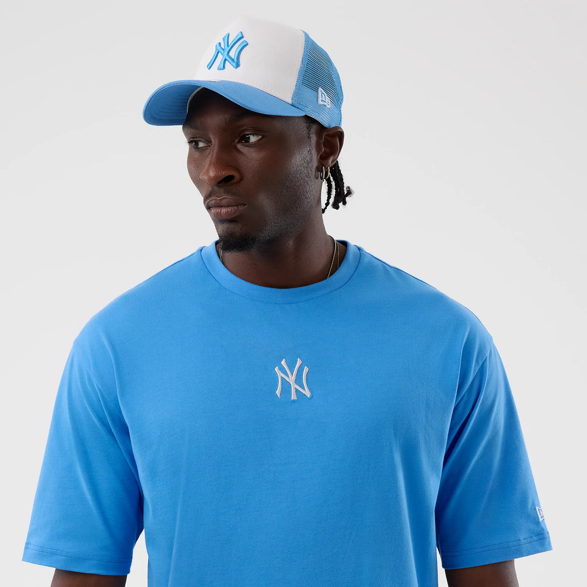New Era New York Yankees MLB League Essential Pastel Blue Oversized T-Shirt, front view on a model with matching cap, displaying the white embroidered New York Yankees logo on the chest and a small New Era flag logo embroidered on the left sleeve.