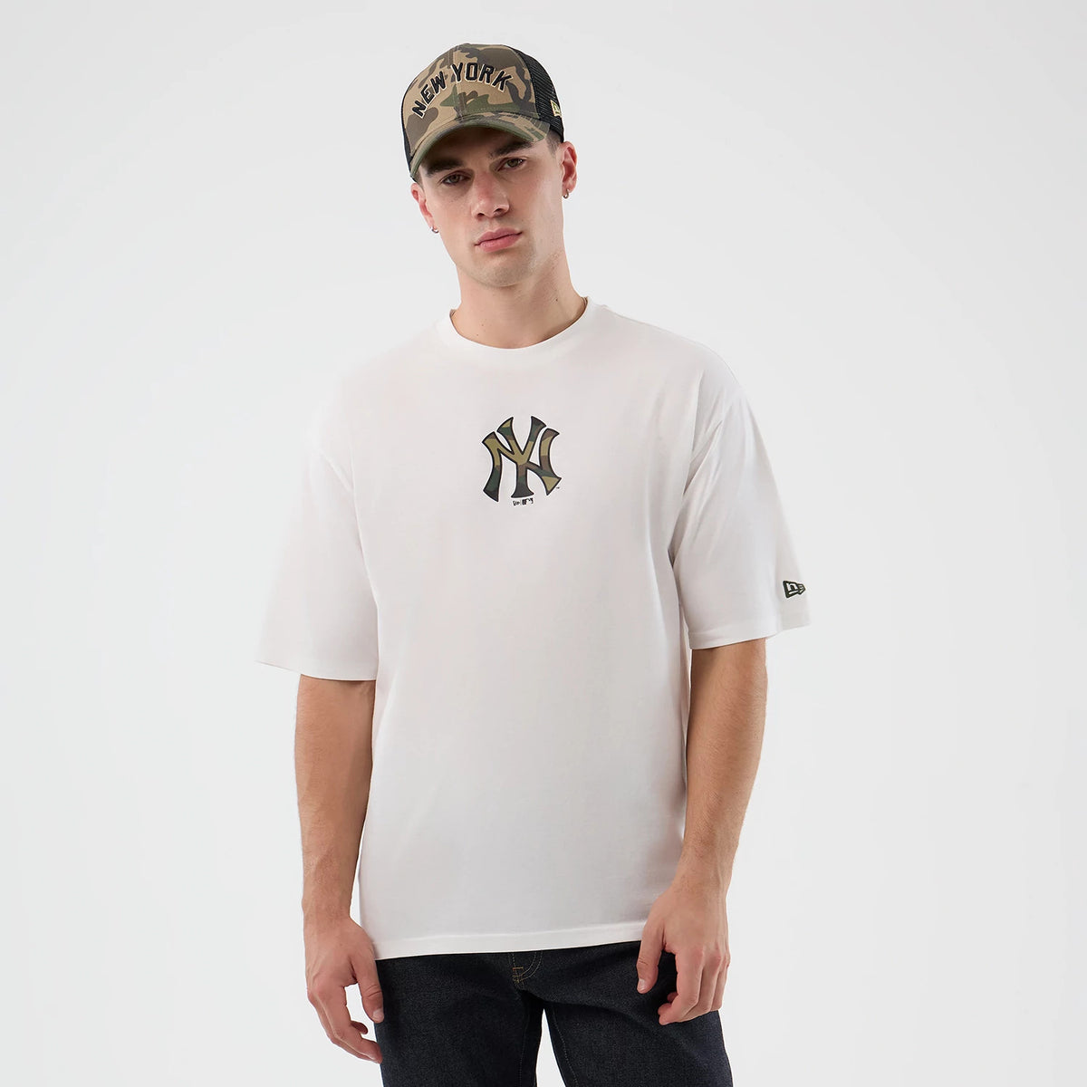 New Era New York Yankees MLB Infill White Oversized T-Shirt, front view on-model showing a large camo-patterned Yankees logo printed at the chest centre, paired casually with dark jeans, and an embroidered New Era flag logo on the left sleeve.