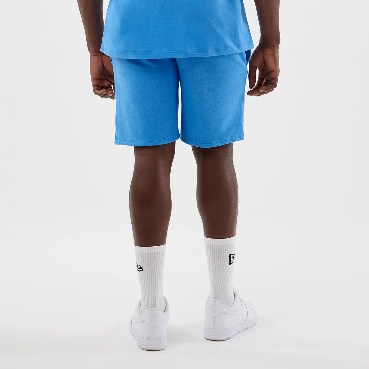 New Era New York Yankees MLB League Essential Pastel Blue Shorts, back view on a model styled with white socks and trainers, showing the plain pastel blue design with a relaxed fit and an elastic waistband.