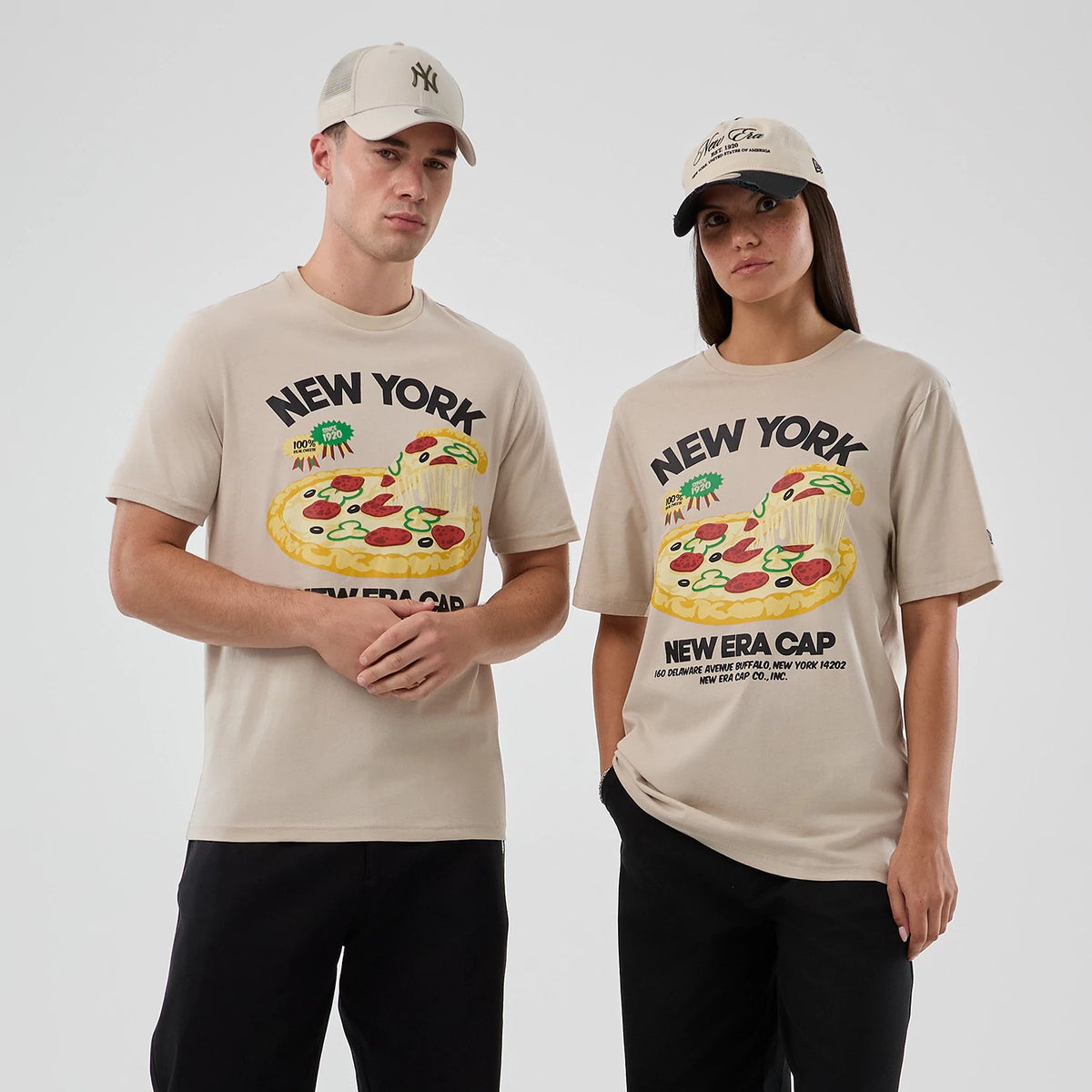 New Era Pizza Graphic Light Beige T-Shirt, front view on model showing a colourful pizza graphic with New York lettering above and New Era Cap script below, paired with a beige cap featuring a curved visor and an embroidered logo.