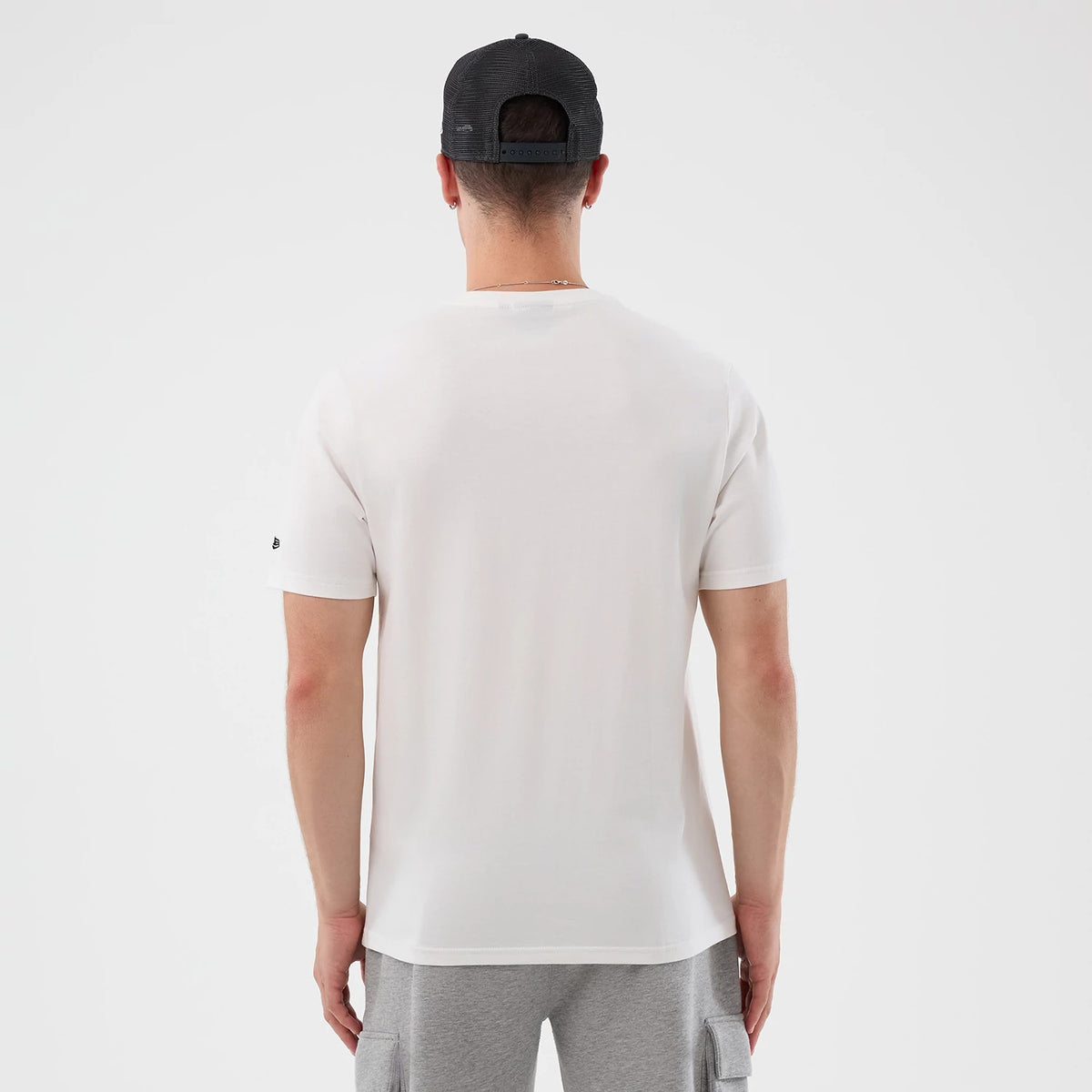 New Era Chicago Bulls NBA Beach Graphic White T-Shirt, back view on-model showing a plain white back with short sleeves, a small embroidered New Era logo on the left sleeve, styled with a back-facing dark cap and grey shorts.