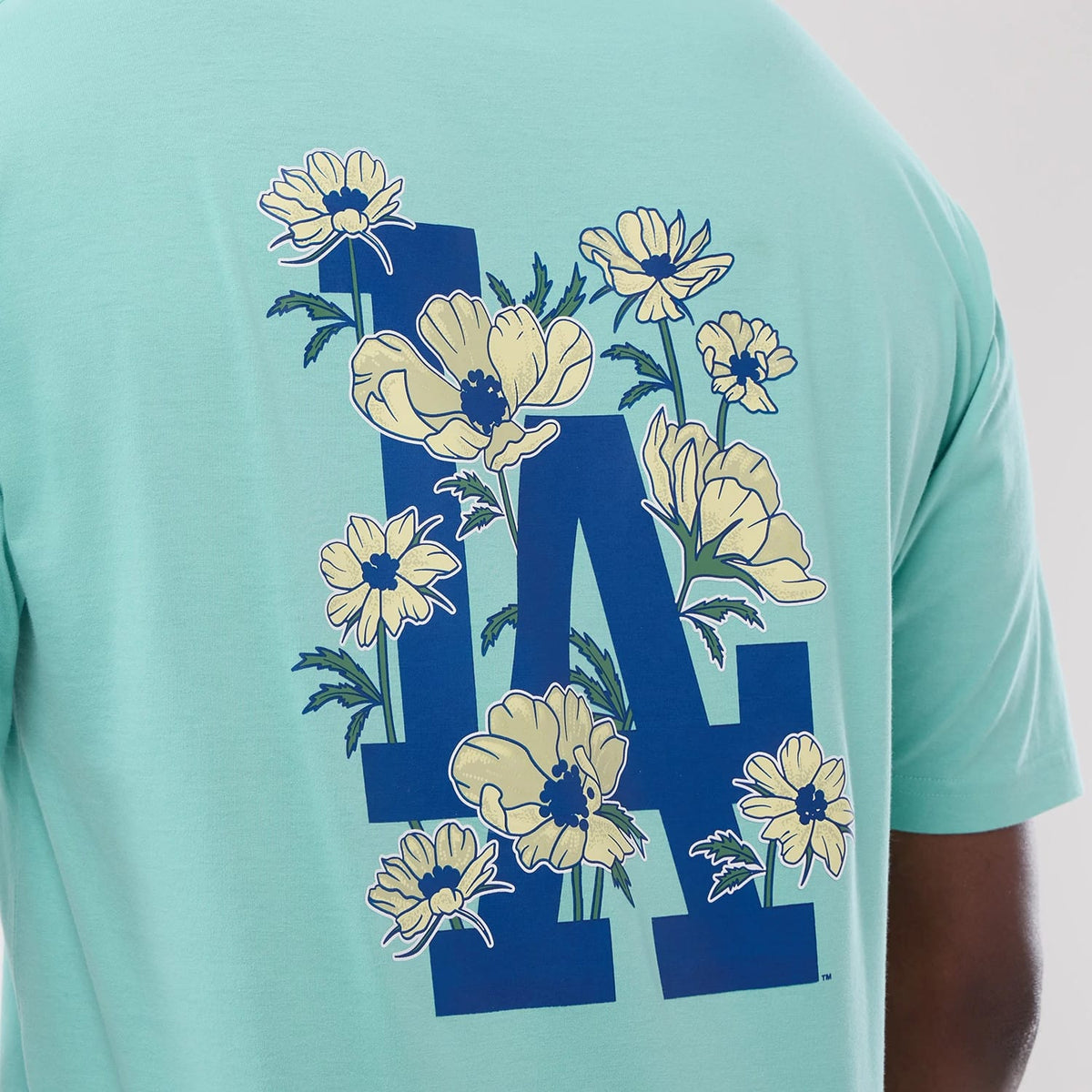 New Era LA Dodgers MLB Floral Pastel Green Oversized T-Shirt, back view showing a model in casual styling and a large blue LA logo adorned with detailed yellow floral graphics covering the entire back centred on the pastel green fabric.