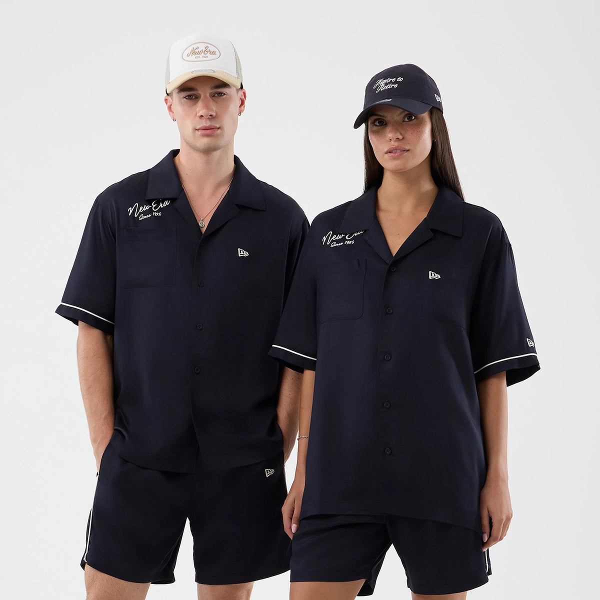 New Era Graphic Revere Navy Short Sleeve Shirt, front view on a model paired with matching navy bottoms, featuring white embroidered New Era script above the left chest pocket, short sleeves with white trim, and black button fastening.