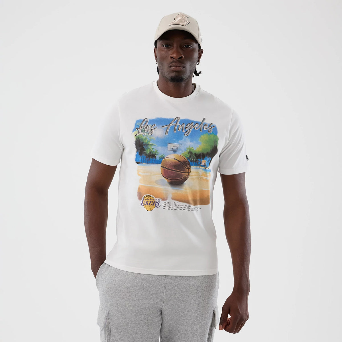 New Era LA Lakers NBA Beach Graphic White T-Shirt, front view on a model, featuring a vivid basketball court scene with palm trees and a basketball at the foreground, Los Angeles text across the chest.