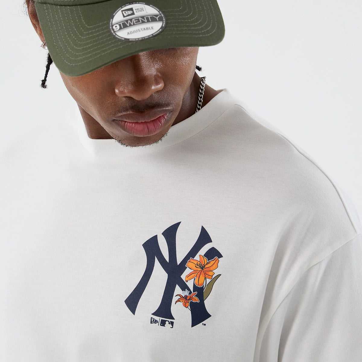 New Era New York Yankees MLB Floral White Oversized T-Shirt, front view on a model with a cap, featuring a large navy embroidered NY logo on the chest embellished with orange floral graphics, shown against the plain white background of the shirt.