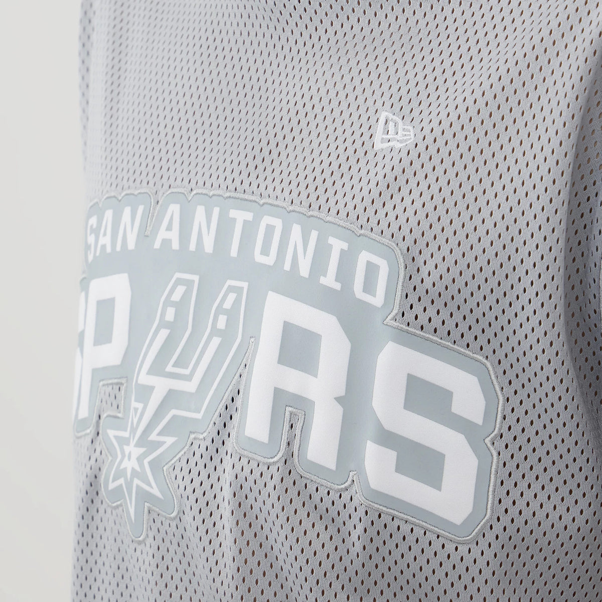 New Era San Antonio Spurs NBA Mesh Grey Oversized T-Shirt, front view showcasing a white printed San Antonio Spurs wordmark across the chest, grey mesh fabric texture, and a small embroidered New Era logo above the graphics on the left side.