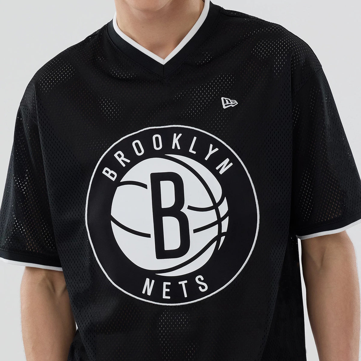 New Era Brooklyn Nets NBA Mesh Black Oversized T-Shirt, front view on-model showing a large central white and black Brooklyn Nets basketball logo, V-neck with white trim, and an embroidered New Era flag logo on the right chest.