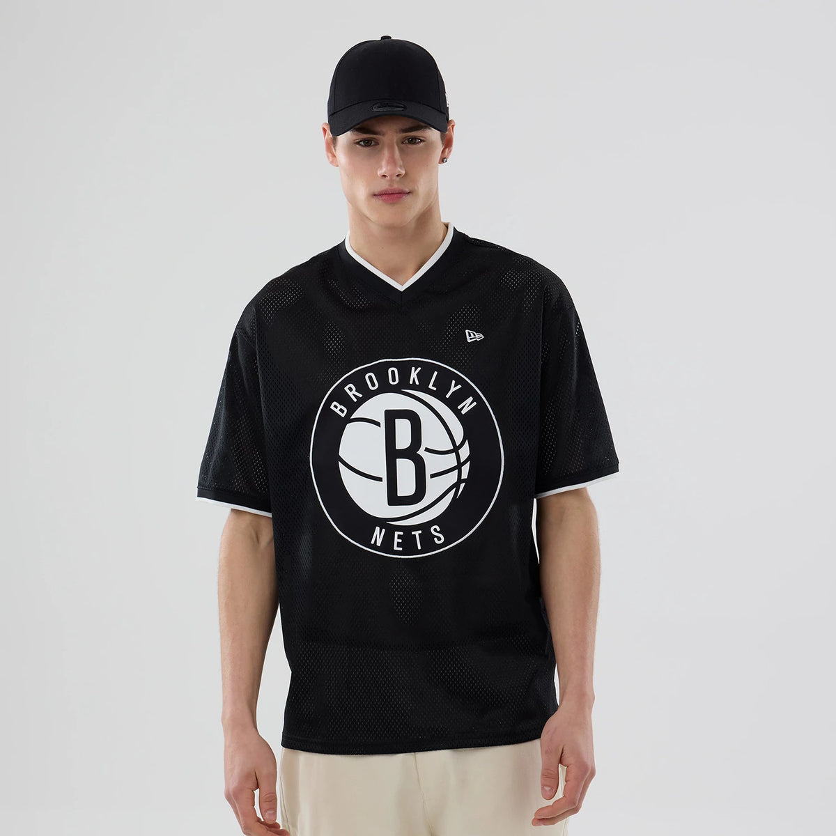 New Era Brooklyn Nets NBA Mesh Black Oversized T-Shirt, front view on a model featuring a large white Brooklyn Nets logo centred on the chest, a small embroidered New Era logo on the left chest, and contrasting white trim on the V-neck collar.