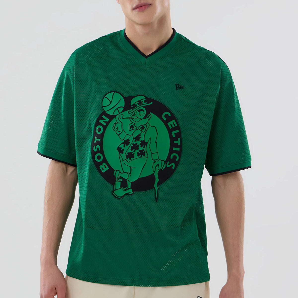 New Era Boston Celtics NBA Mesh Green Oversized T-Shirt, front view on a model featuring a large Celtics graphic with a basketball player in the centre of the chest, black mesh trim around the collar and sleeves.