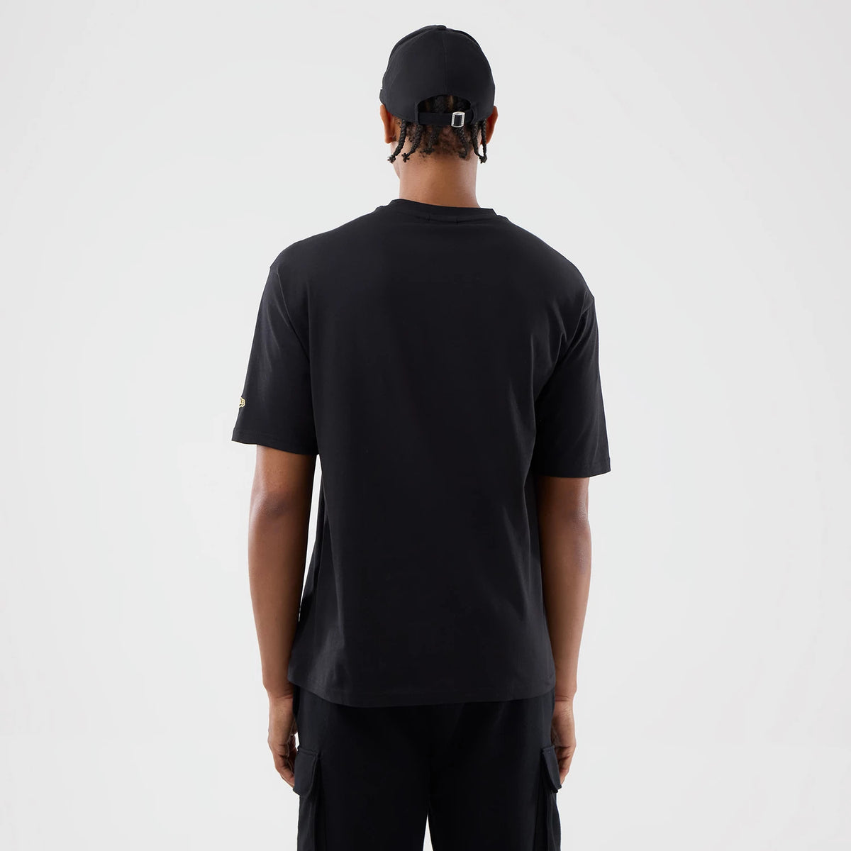 New Era Sticker Copenhagen Black Oversized T-Shirt, back view on a model pairing it with black trousers and a black cap, showcasing a plain back with short sleeves and an embroidered New Era logo on the left sleeve.