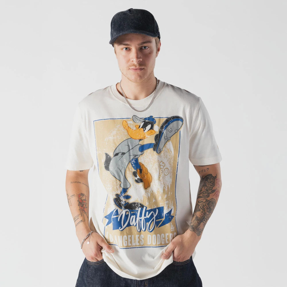 New Era LA Dodgers MLB X Looney Tunes Cream T-Shirt, front view on a model styled with a dark cap, featuring a large cartoon graphic of Daffy Duck in a baseball uniform, with Daffy lettering above Los Angeles Dodgers text at the bottom.