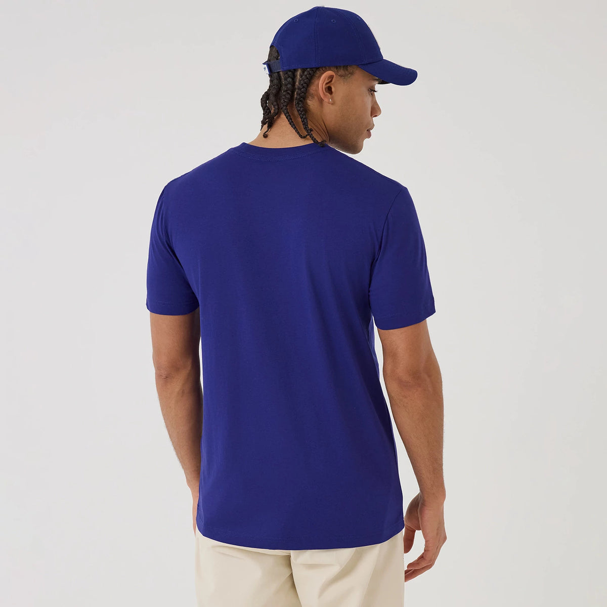 New Era LA Dodgers MLB X Looney Tunes Dark Blue T-Shirt, back view on a model showing a plain dark blue surface with short sleeves and a crew neckline, styled with a matching dark blue cap and light-coloured trousers for a cohesive look.