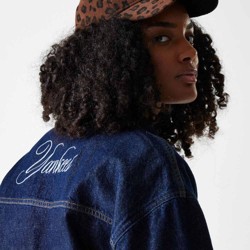 New Era New York Yankees Womens MLB Denim Dark Blue Jacket, back view on a model styled with a leopard print cap, showing Yankees in elegant embroidered script across the upper back of the dark blue denim fabric.