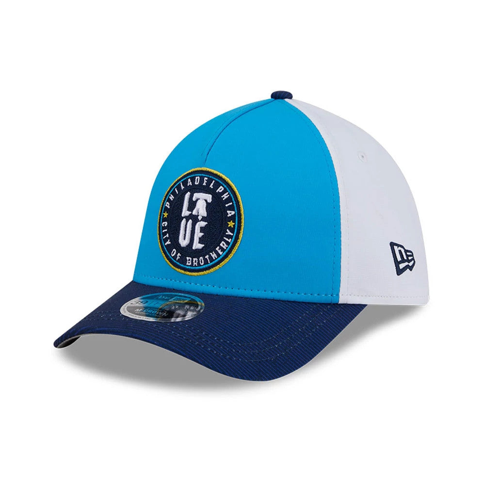 Phillies MLB City Connect Blue New Era 39THIRTY M-Crown A-Frame Stretch Fit Cap, three-quarter view showing the circular 'Philadelphia City of Brotherly Love' logo embroidered in yellow and white on the front panel, with a blue curved visor.