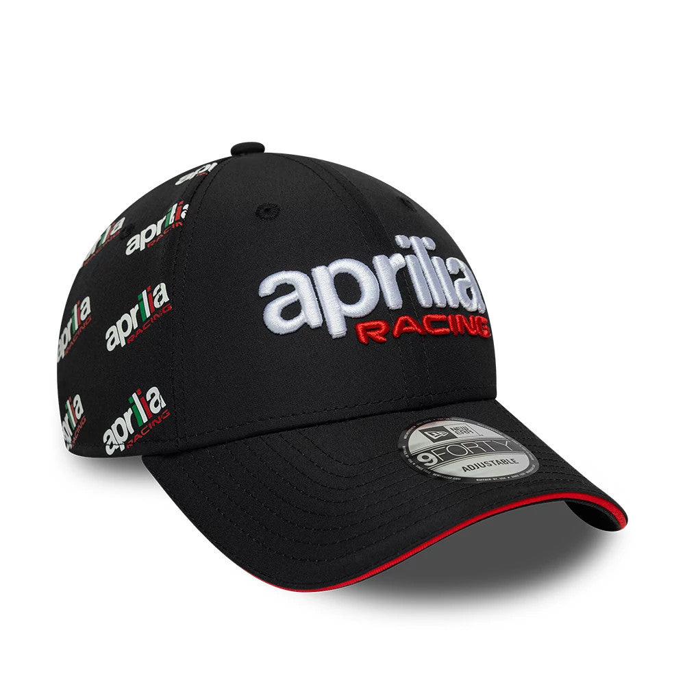 Aprilia All Over Print Black New Era 9FORTY Adjustable Cap, three-quarter view showing white embroidered aprilia and red RACING logo on the front panel, multicoloured logos on the side, black curved visor with red edge, and 9FORTY size sticker.