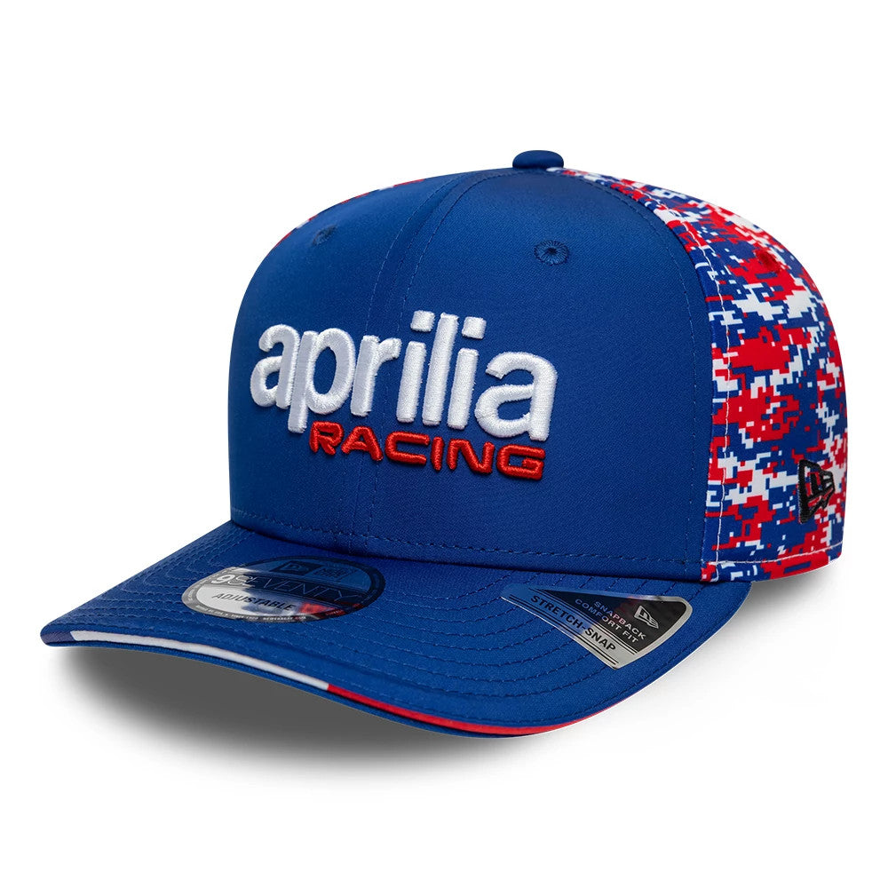 Aprilia Replica Le Mans Race Special Blue New Era 9SEVENTY Stretch Snap Adjustable Cap, three-quarter view showing the raised white and red embroidered aprilia racing logo on the blue front panel, with digital camo side panels.
