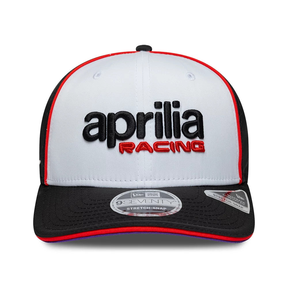 Aprilia Team White New Era 9SEVENTY Stretch Snap Adjustable Cap, front view showing black and red embroidered Aprilia Racing logo on white front panel, with black visor featuring a 9SEVENTY size sticker and red piping along the edges.