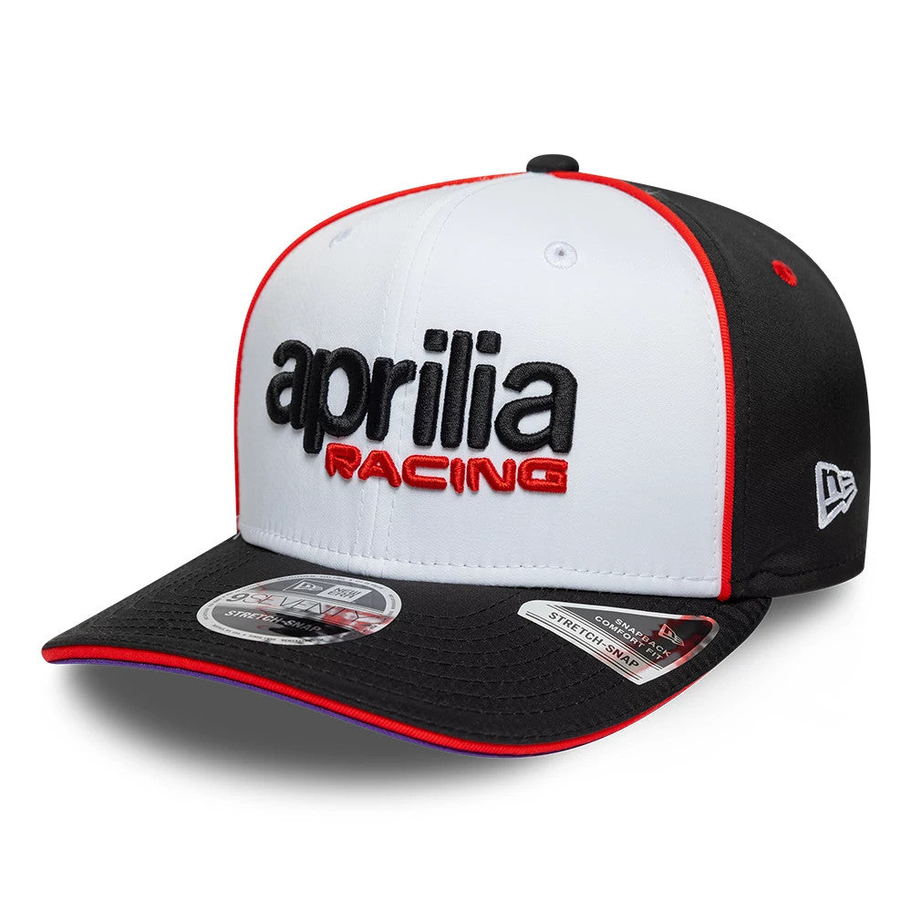 Aprilia Team White New Era 9SEVENTY Stretch Snap Adjustable Cap, front view showing the large black and red embroidered aprilia RACING logo on the white front panel, contrasting black visor with red trim, and 9SEVENTY size sticker.
