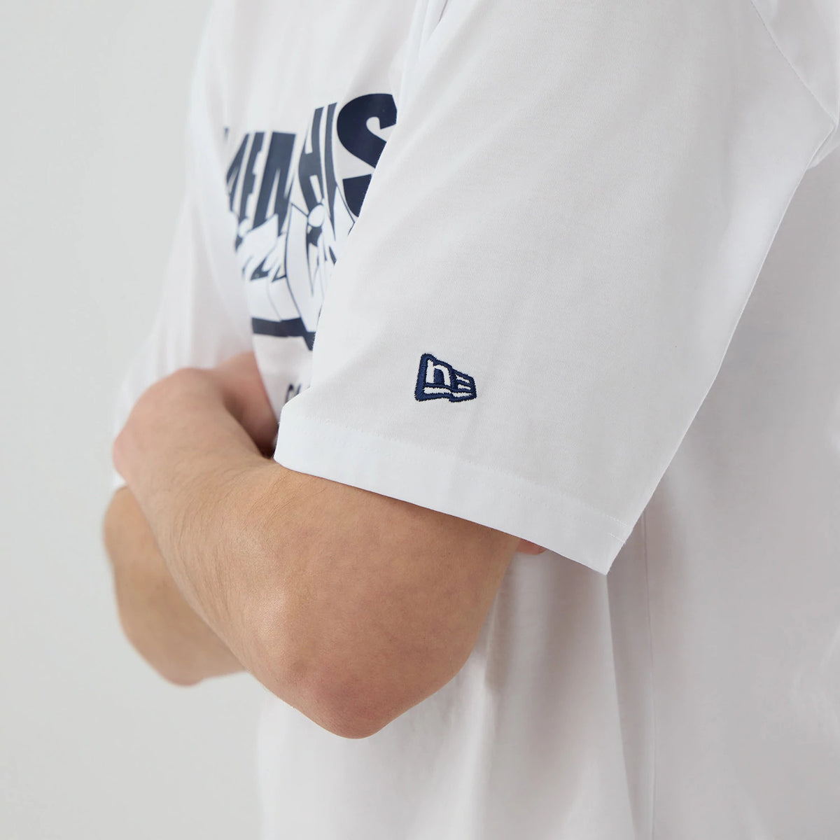 New Era Memphis Grizzlies NBA London Game 2026 White Oversized T-Shirt, three-quarter view showing the navy printed Grizzlies graphic across the chest, worn on a model with crossed arms, and an embroidered New Era flag on the left sleeve.