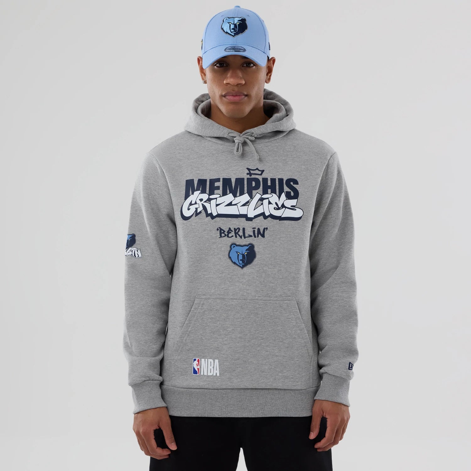 New Era Memphis Grizzlies NBA Berlin Game 2026 Grey Pullover Hoodie, front view on-model showing the large printed Memphis Grizzlies and Berlin graphics across the chest, an embroidered Grizzlies logo on the left sleeve.