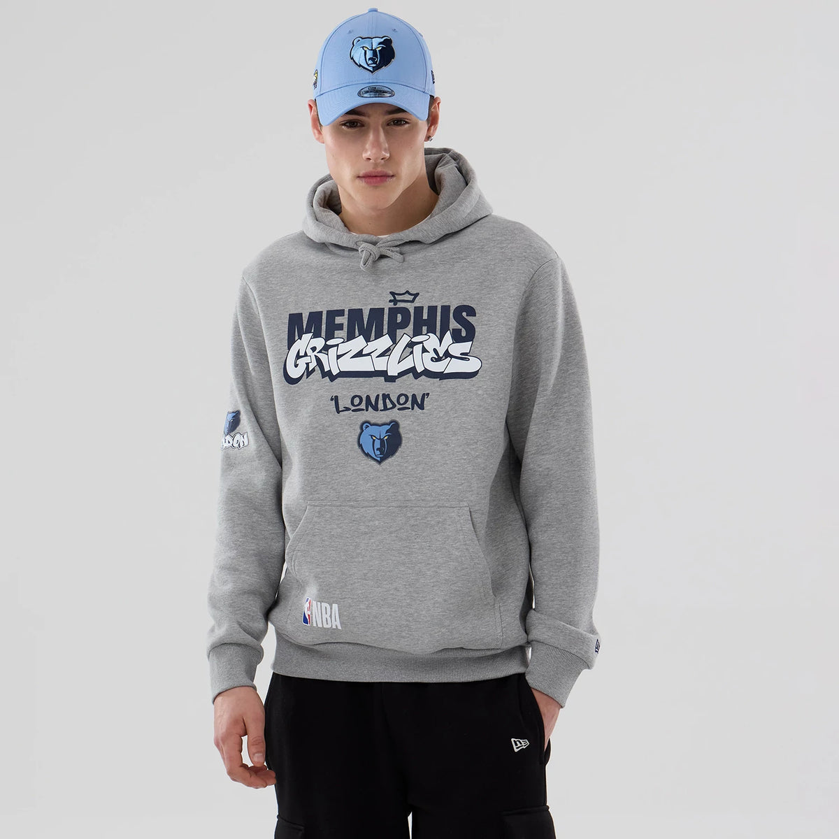 New Era Memphis Grizzlies NBA London Game 2026 Grey Pullover Hoodie, front view on a model wearing a light blue cap, showing the Memphis Grizzlies lettering across the chest, an embroidered bear logo below.