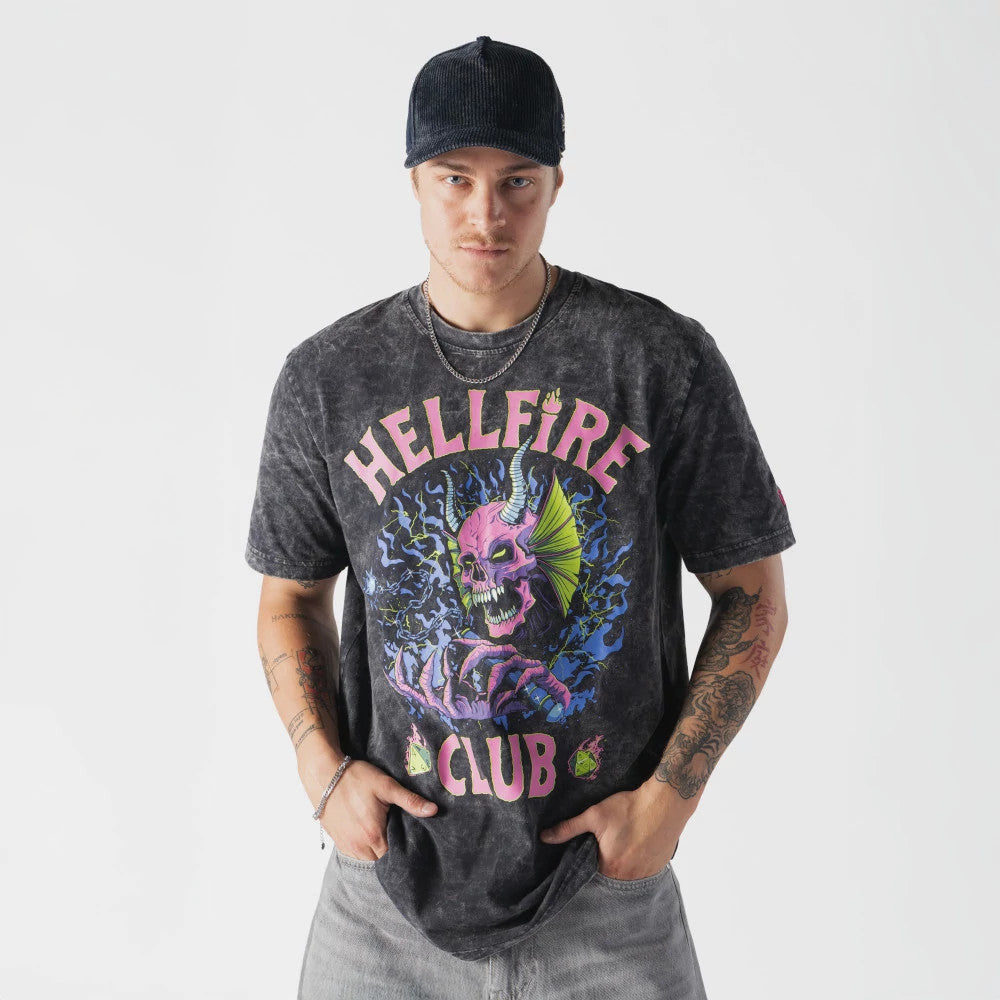 New Era Netflix Stranger Things Hell Fire Club Black T-Shirt, front view on-model showing a graphic of a purple horned skull with green eyes at the centre, with pink Hellfire Club lettering above and below, styled with light jeans.