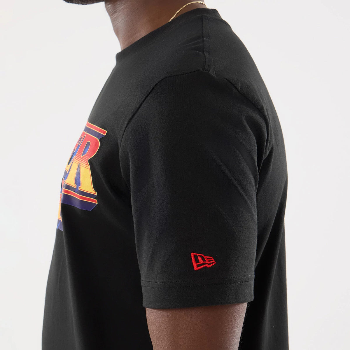New Era Netflix Stranger Things Black T-Shirt, side view showing a colourful printed graphic on the chest, a red embroidered New Era logo on the sleeve, and the simple black tee styled on a model.