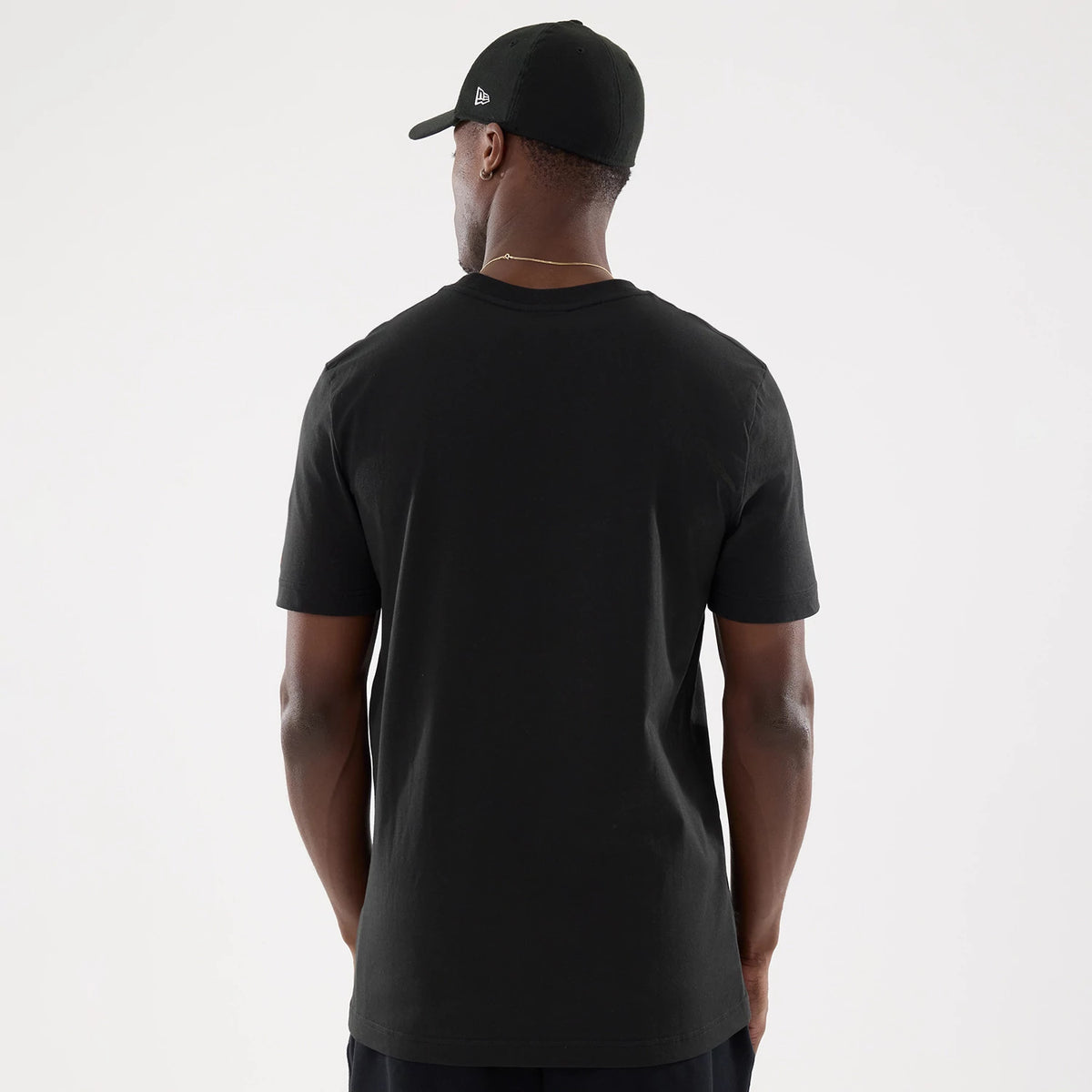 New Era Netflix Stranger Things Black T-Shirt, back view on a model showing the plain black fabric with a simple round collar, short sleeves extending to the upper arm, and paired with a black cap featuring an embroidered New Era logo on the side.
