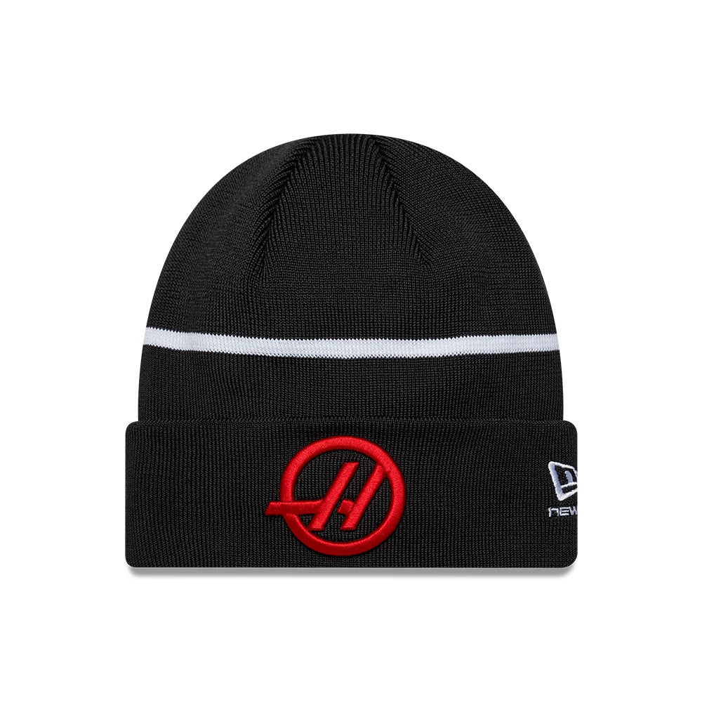 New Era TGR Haas F1 Oliver Bearman Black Cuff Knit Beanie Hat, front view showing a raised red HAAS logo embroidered on the fold-over cuff, a white stripe running horizontally around the crown, and the New Era flag logo in white on the side.