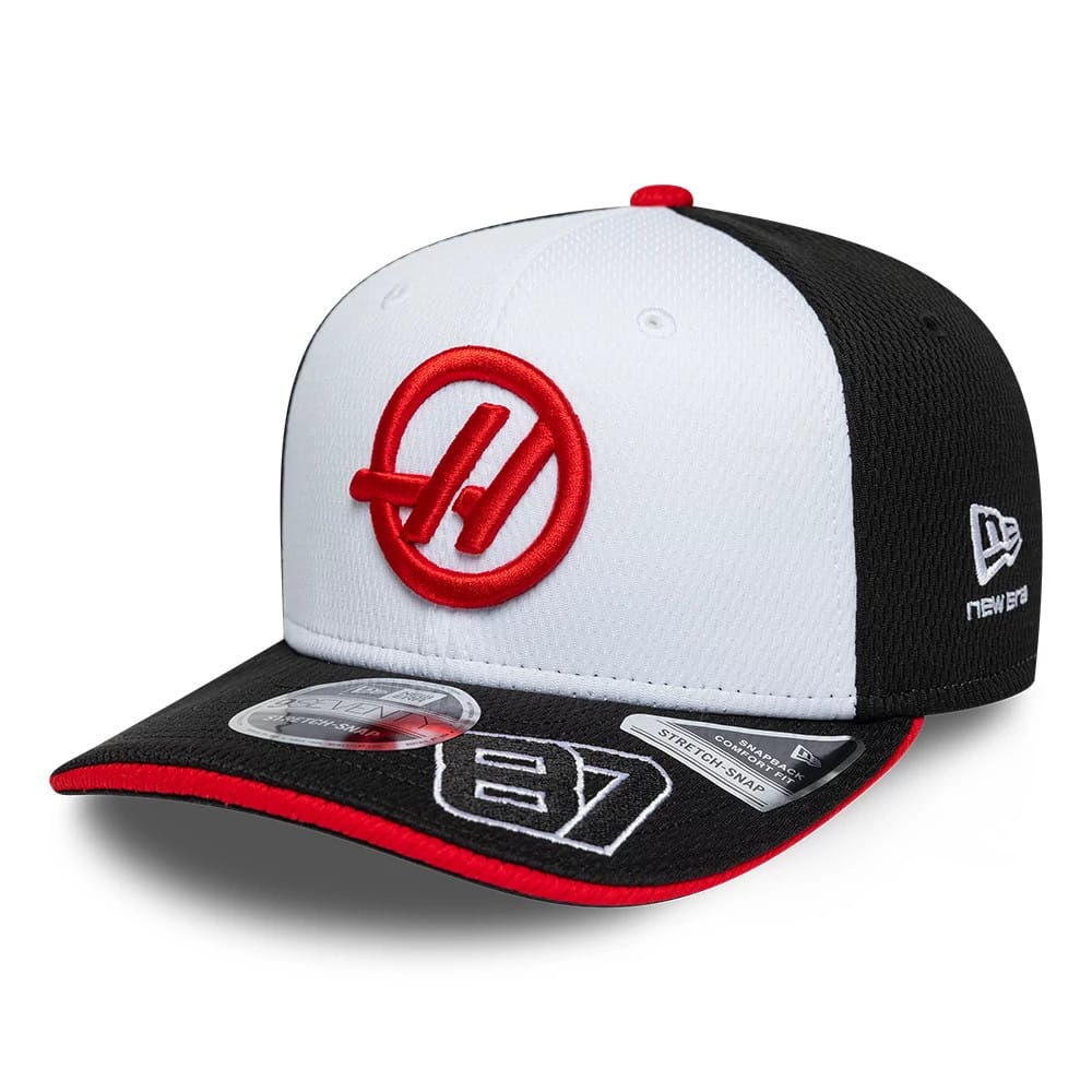 TGR Haas F1 Oliver Bearman Black New Era 9SEVENTY Stretch Snap Cap, three-quarter view showing the red circle logo with a stylised H on the white front panel, black visor with grey 87 embroidery, and New Era flag on the left side.