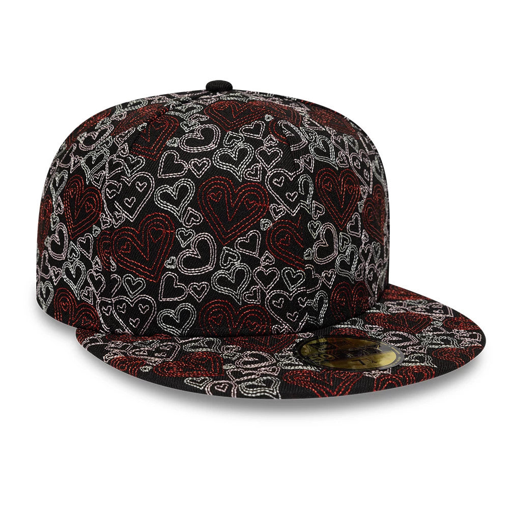 New Era All Over Hearts Black 59FIFTY Fitted Cap, front view showing a detailed pattern of red and white embroidered hearts covering the structured black crown and flat visor, with a gold 59FIFTY size sticker on the visor.