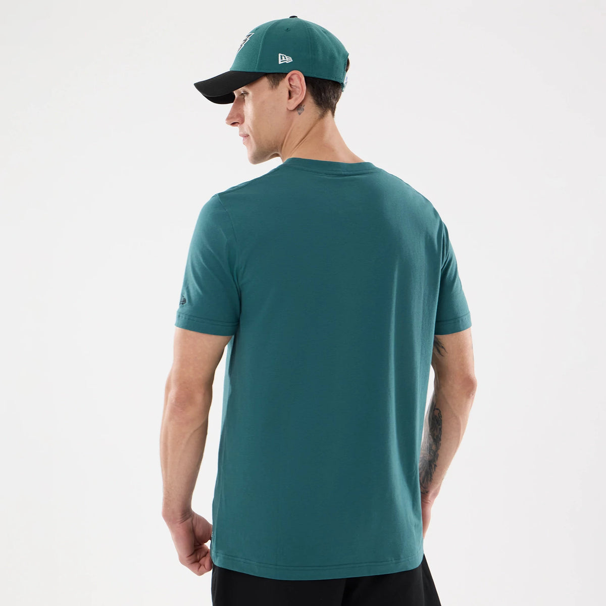 New Era Philadelphia Eagles NFL Training 2026 Dark Green T-Shirt, back view on a model styled with a matching cap, showing a plain dark green back with an embroidered logo on the left sleeve near the hem and short sleeves.