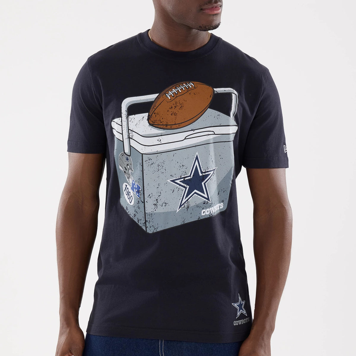 New Era Dallas Cowboys NFL Training 2026 Navy T-Shirt, front view on a model showing a large graphic of an ice chest with a football on top on the chest, a printed Cowboys star logo beneath, and a smaller star logo near the left hem.